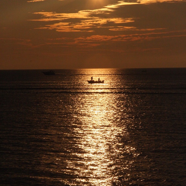 Reflection of sunset over calm water out to horizon line and up into the clouds.